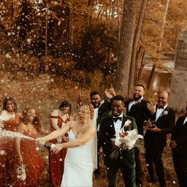 Bride spraying champagne in celebration while the groom and wedding party cheer by the Little Miami River.