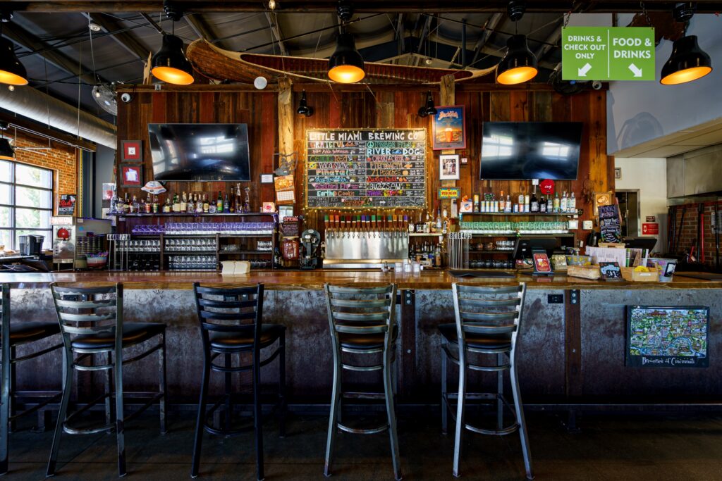 Little Miami Brewing Company’s interior with wooden counters, beer taps, TVs, and a chalkboard menu.