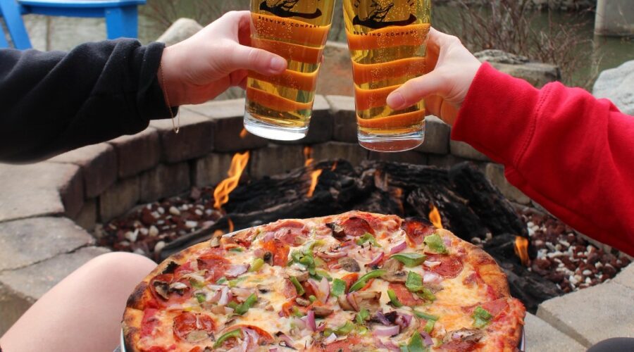 A couple clinking their beer glasses on a riverside brewery date at Little Miami Brewing Company.