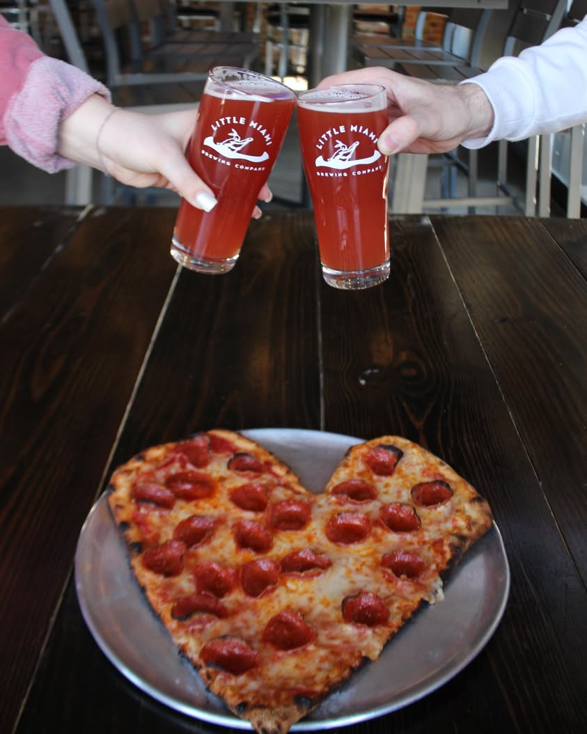 A couple celebrating Valentine’s Day with beers and a heart-shaped pepperoni pizza at Little Miami Brewing Company.