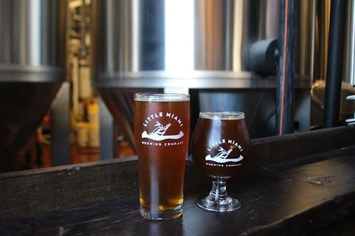 Two freshly poured craft beers displayed with stainless steel fermentation tanks inside Little Miami Brewing Company.