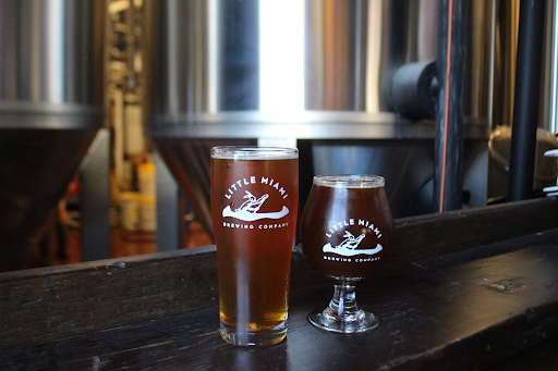 Two freshly poured craft beers in Little Miami Brewing Company branded glasses on a brewery table.
