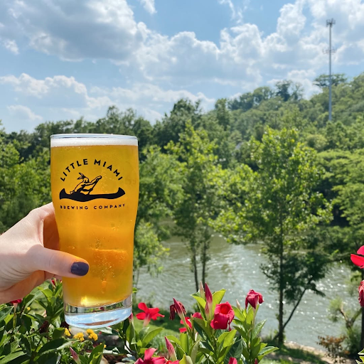 Hand holding a pint of Addie's Ale outdoors overlooking the Little Miami River at Little Miami Brewing Company.