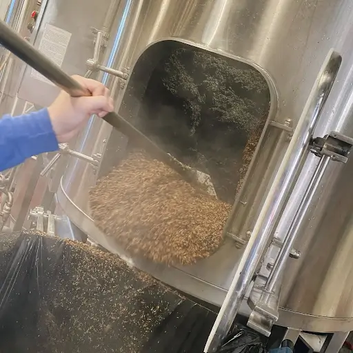 Brewer removing spent grain from a stainless steel mash tun during the brewing process at Little Miami Brewing Company.