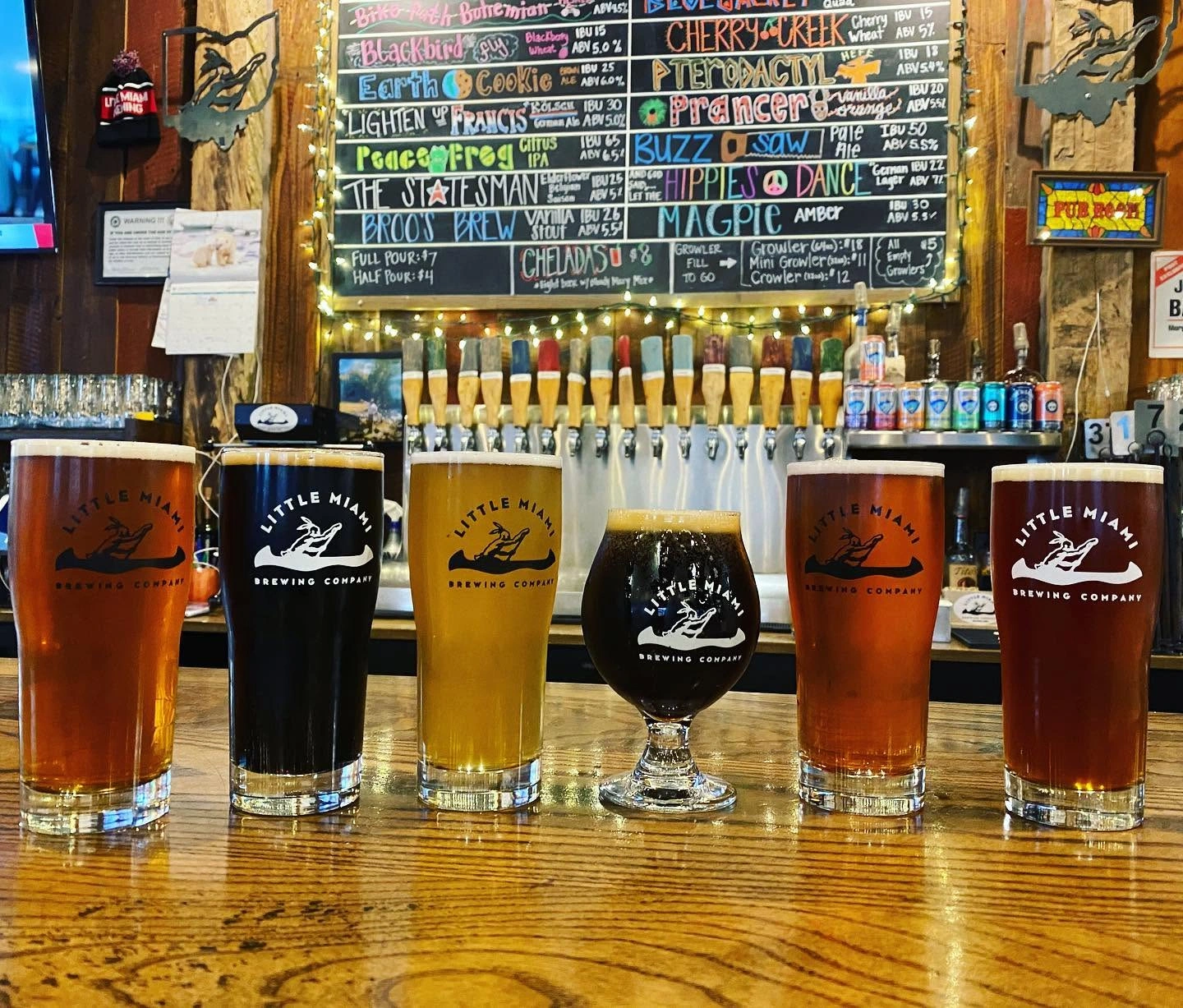 A colorful lineup of craft beers with varying colors on the counter at Little Miami Brewing Company.