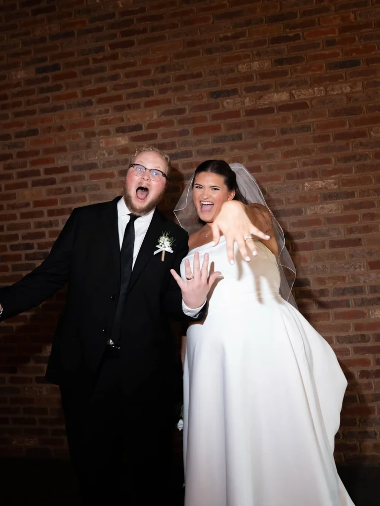 A newly engaged couple smiling and flaunting their rings indoors at the Little Miami Brewing Company Event Center.