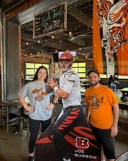 Fans in sports gear celebrating next to a player cutout inside the Little Miami Brewing Company.