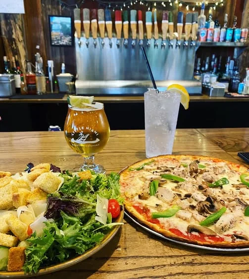 Gluten-free green salad, a loaded pizza, and two beverages on a counter with tap handles at Little Miami Brewing Co.